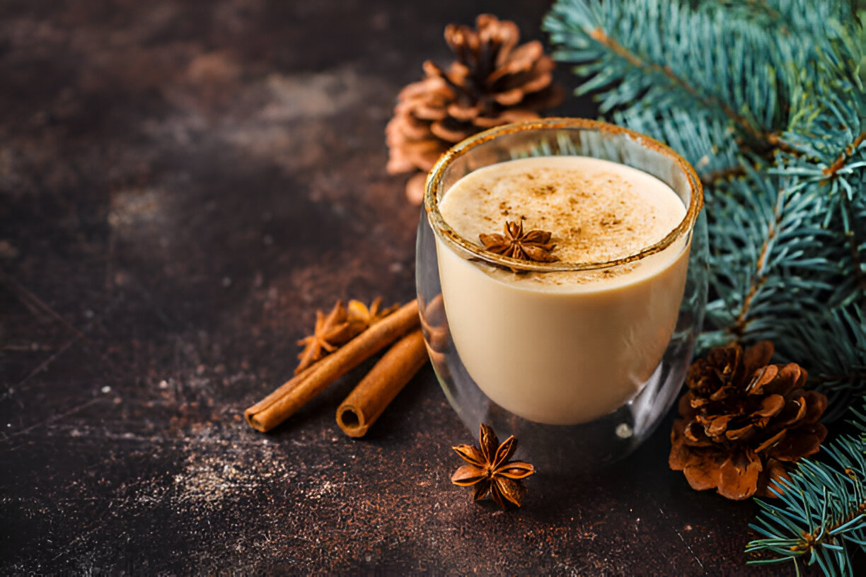 A cozy drink with spices in a glass, surrounded by pine cones and cinnamon sticks on a dark surface.