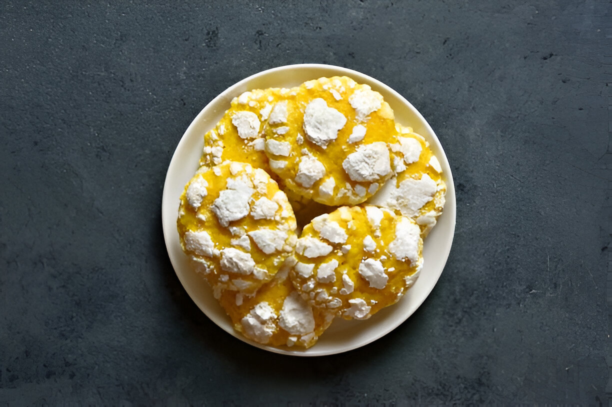 A plate of yellow cookies with white powdered coating, arranged neatly on a dark surface.