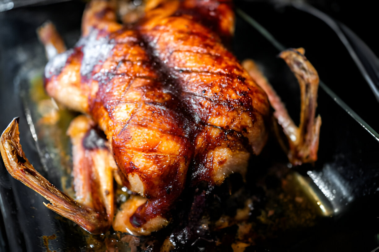 A roasted whole chicken with crispy skin resting in a glass baking dish.