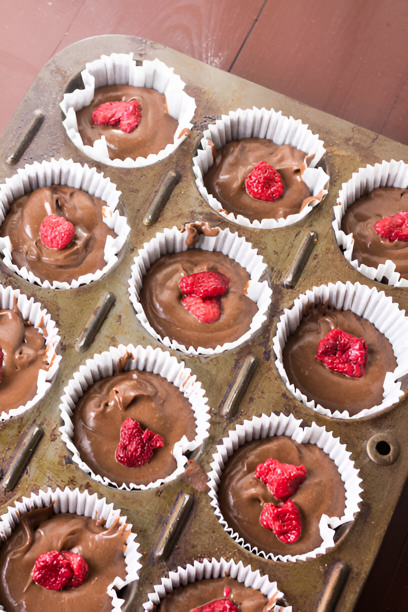 A tray of unbaked chocolate cupcakes topped with pieces of raspberry.