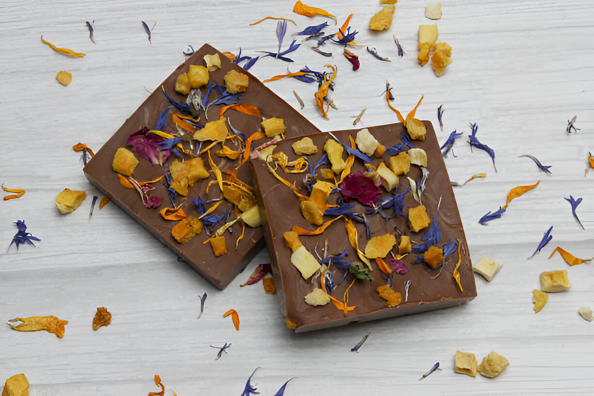 Two beautifully decorated chocolate bars garnished with dried flowers and fruit pieces on a light wooden background.