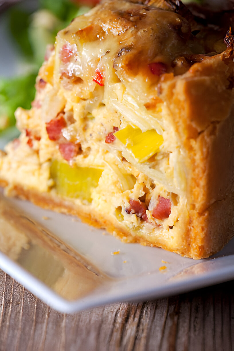 Close-up of a slice of savory baked dish with a golden crust, filled with mixed vegetables and meats.