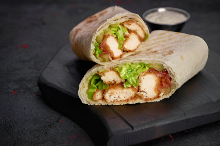 Two halves of a crispy chicken wrap with lettuce and sauces on a black plate.