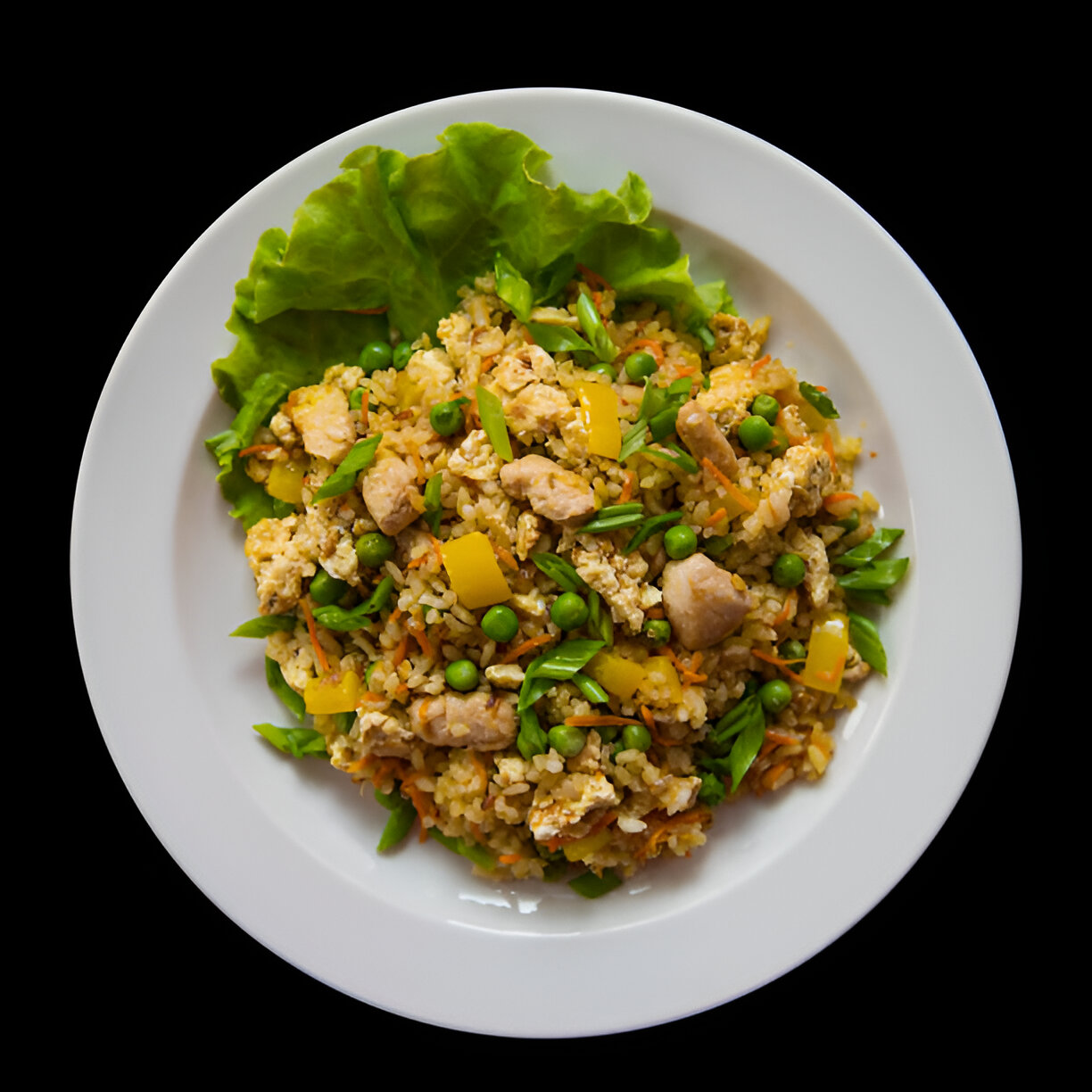 A delicious plate of fried rice with chicken, peas, bell peppers, and green onions, served on a white plate with leafy greens.