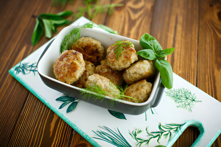 A bowl of meatballs garnished with herbs, placed on a vibrant green leaf-patterned cutting board.