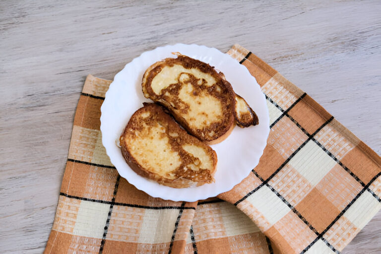 Two slices of golden-brown French toast on a white plate, placed on a checkered cloth