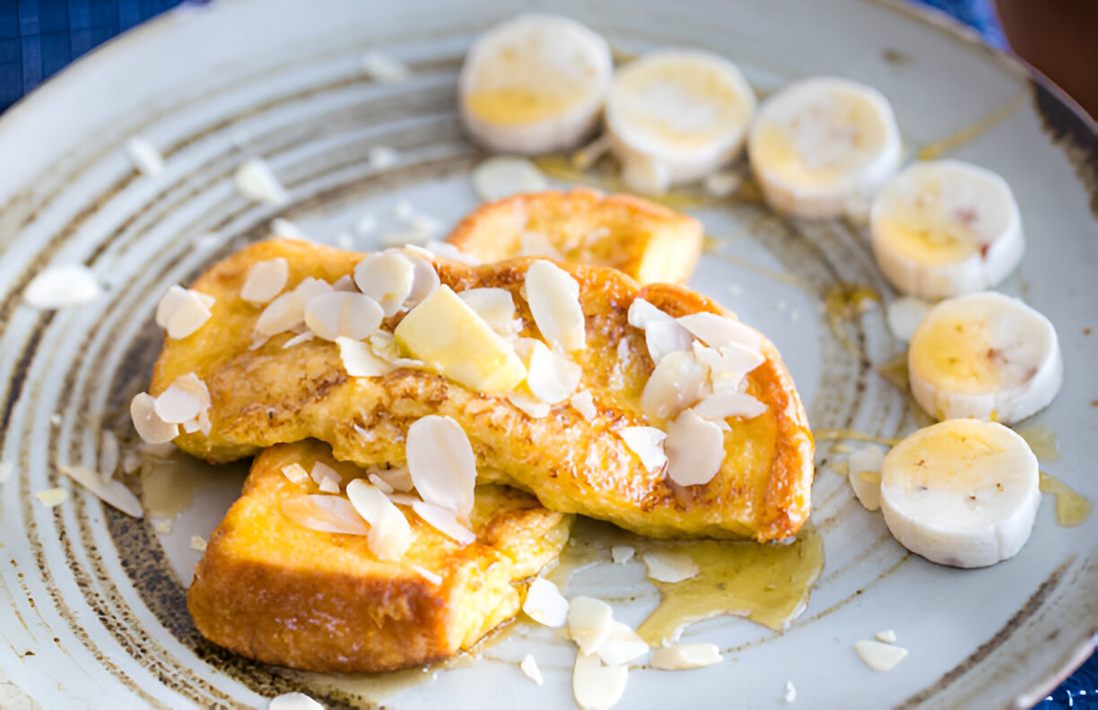 A plate of French toast topped with almond slices and a pat of butter, accompanied by banana slices.