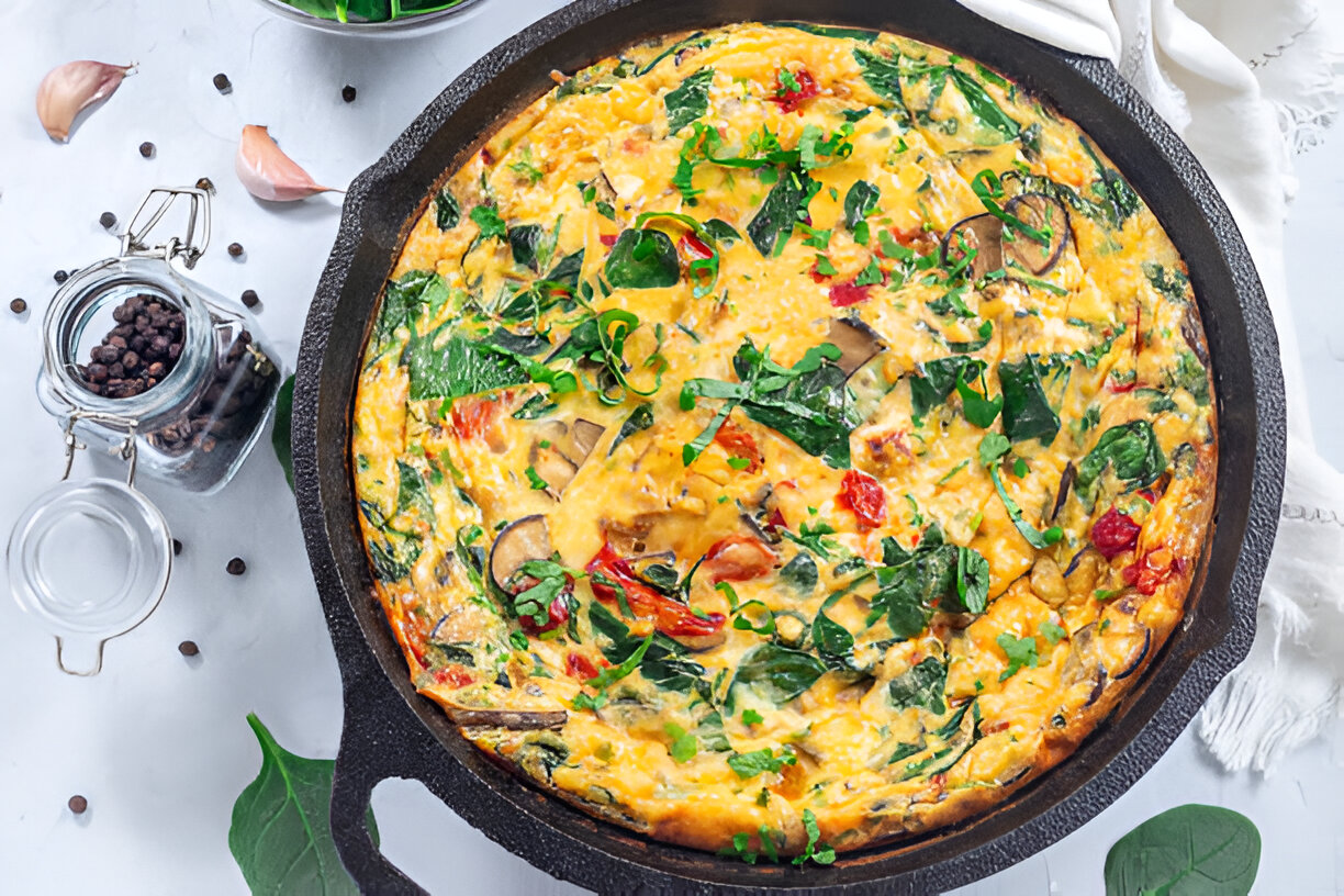A skillet filled with a colorful vegetable frittata, featuring spinach, tomatoes, and herbs.