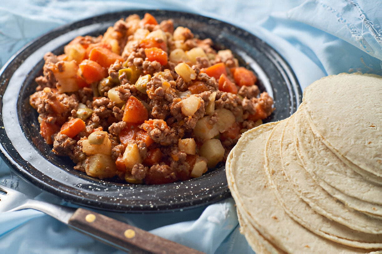 A plate of ground beef mixed with vegetables, served alongside stack of tortillas.