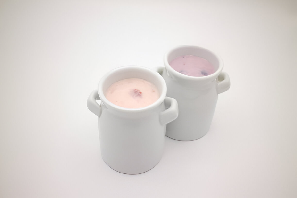 Two white ceramic cups filled with yogurt on a plain background.