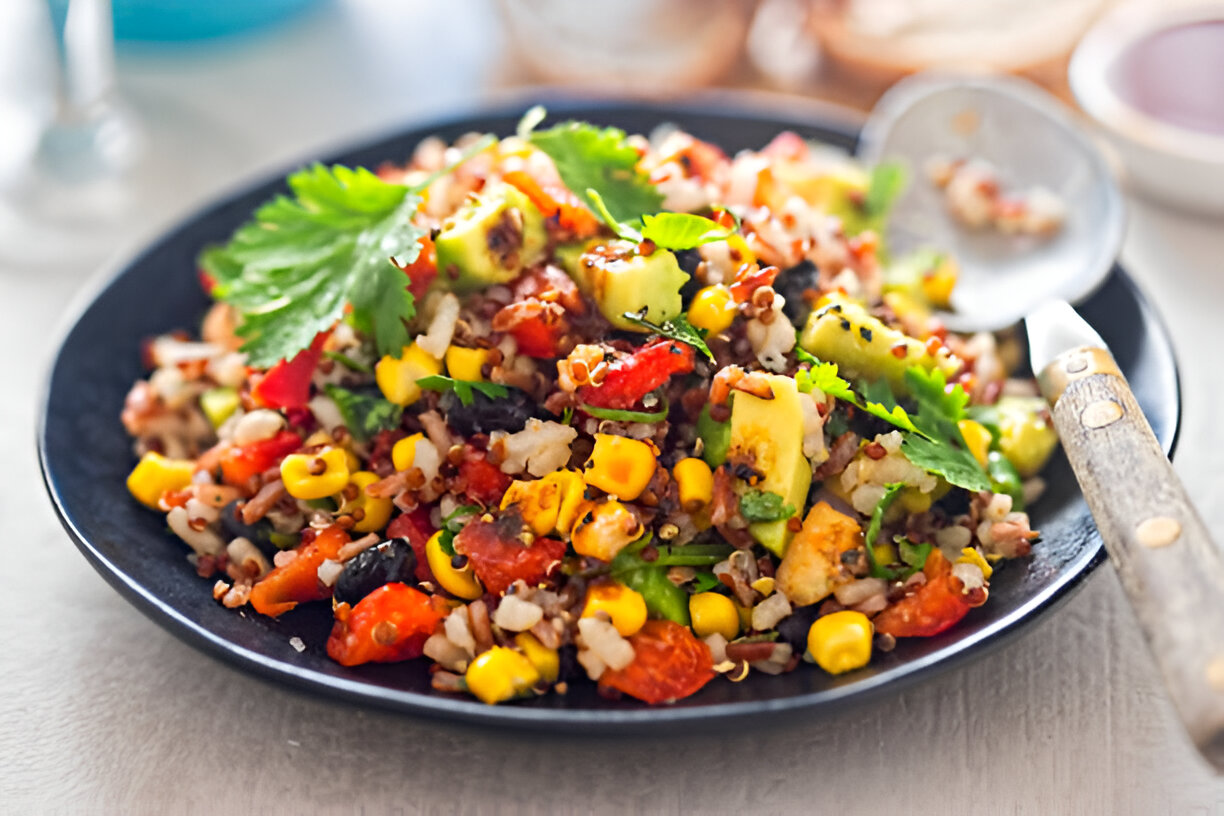 A vibrant quinoa salad with black beans, corn, chopped vegetables, and cilantro served in a black bowl.