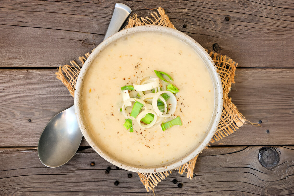 A bowl of creamy soup garnished with green onion slices, placed on a rustic wooden surface.