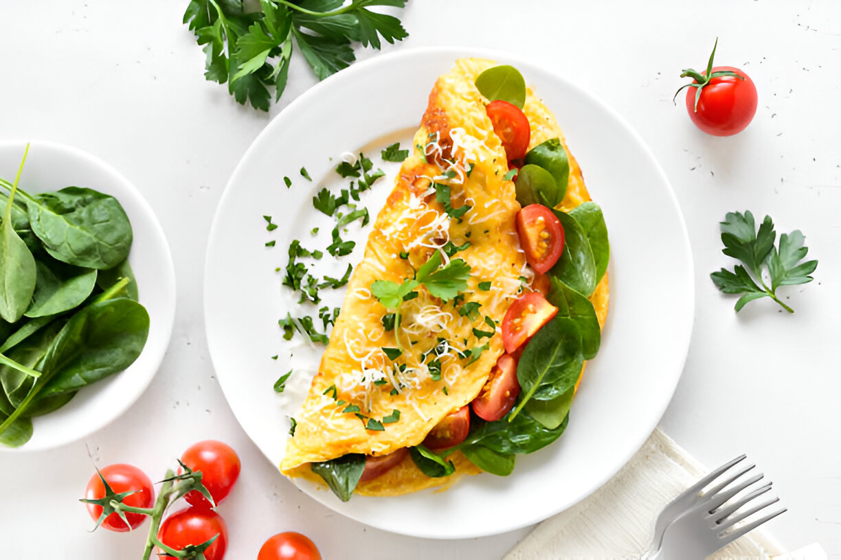 A delicious omelette filled with spinach and cherry tomatoes, garnished with parsley and cheese, served on a white plate.