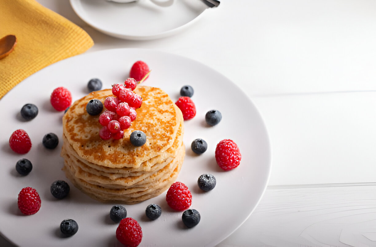 A stack of fluffy pancakes topped with fresh berries including raspberries, blueberries, and red currants, arranged on a white plate.