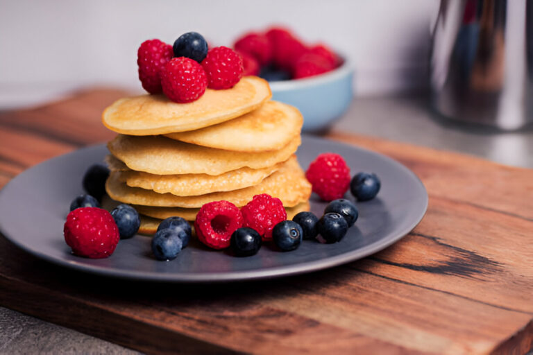 Stack of pancakes topped with fresh raspberries and blueberries on a gray plate