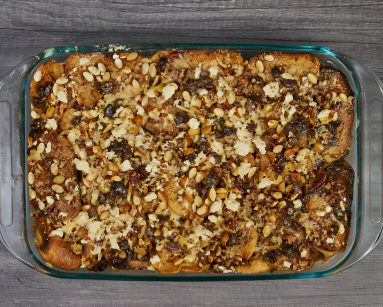 A baked dish with a golden-brown crust topped with nuts and dried fruits in a glass baking dish.