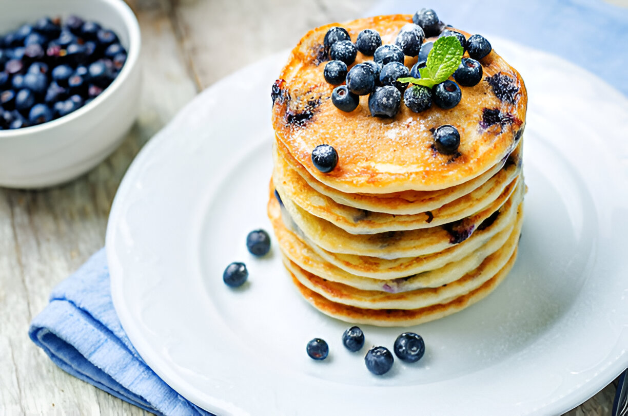A stack of pancakes topped with blueberries and a sprig of mint on a white plate.