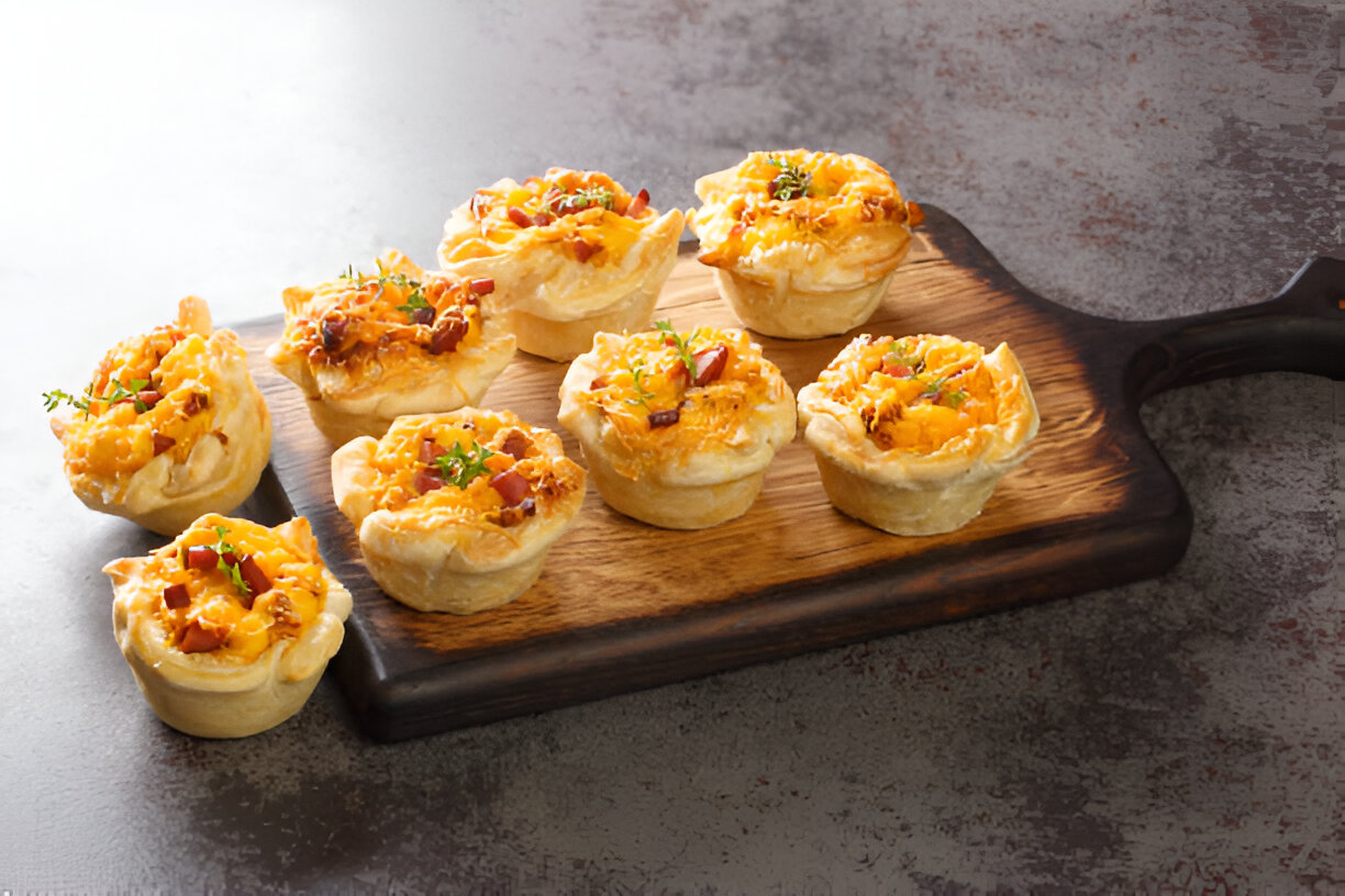 Delicious mini savory pies topped with cheese and herbs on a wooden serving board.