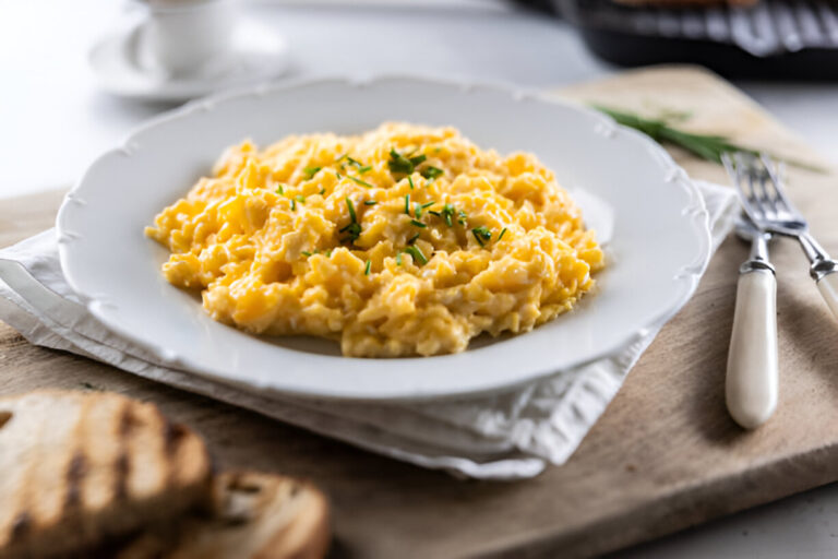 A plate of creamy scrambled eggs garnished with chives, served with slices of toasted bread.