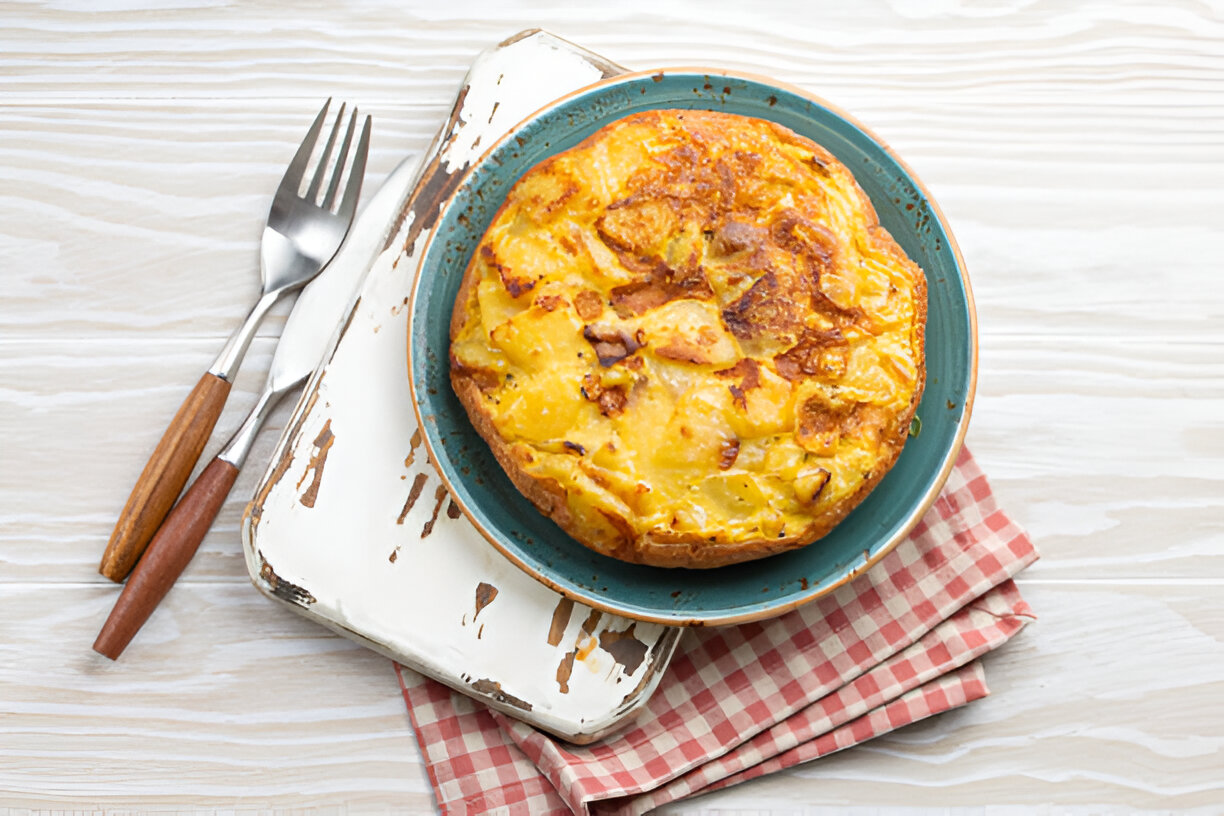 A plate of Spanish tortilla on a rustic surface with a fork and knife nearby.