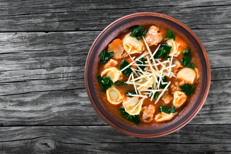 A hearty bowl of soup featuring tortellini, greens, and shredded ginger, served in a brown bowl on a wooden table.