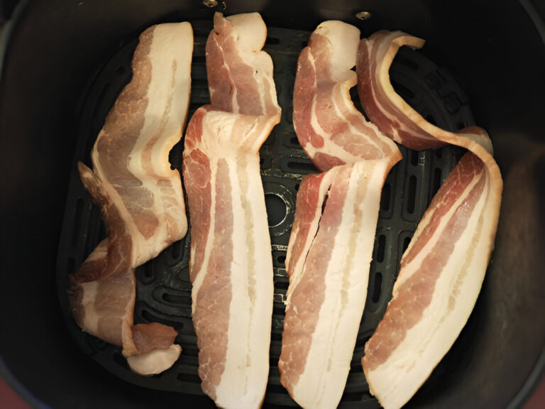 Raw bacon strips arranged in an air fryer basket