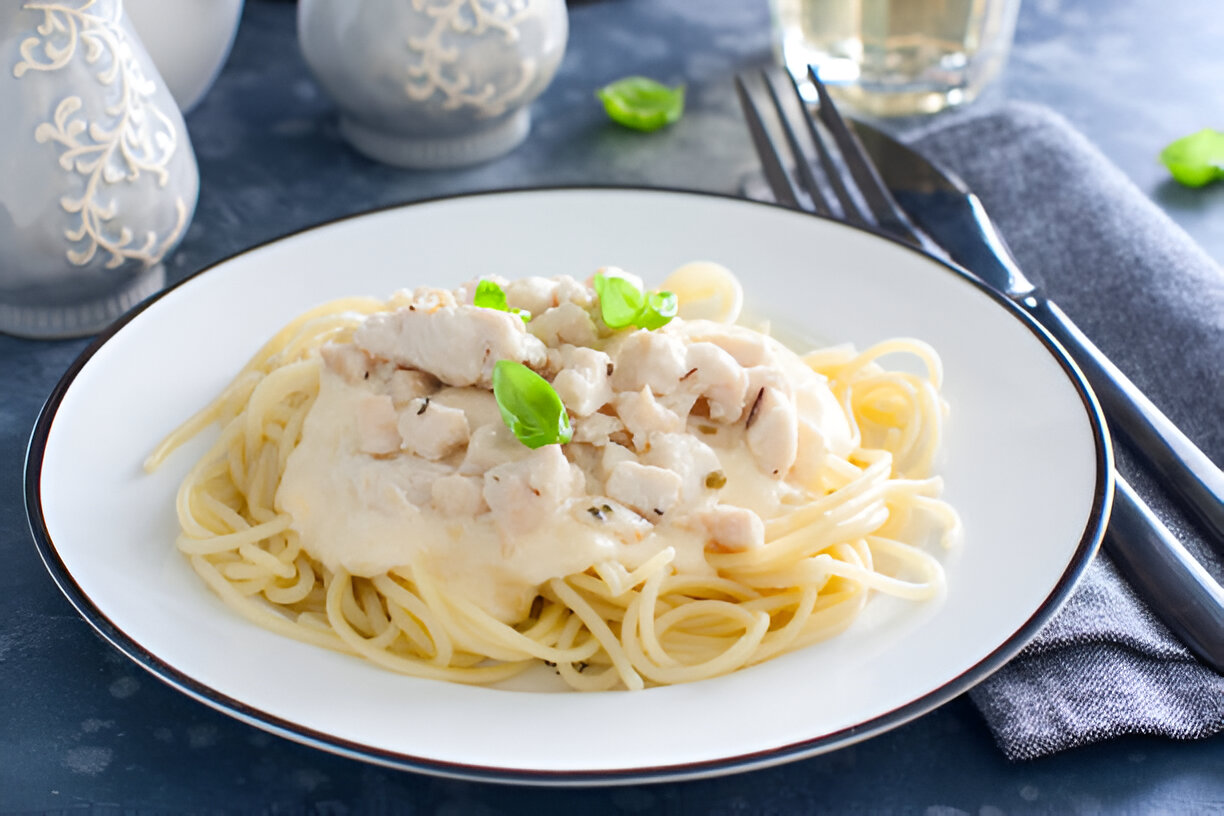 A plate of spaghetti topped with a creamy chicken sauce and garnished with fresh basil leaves.