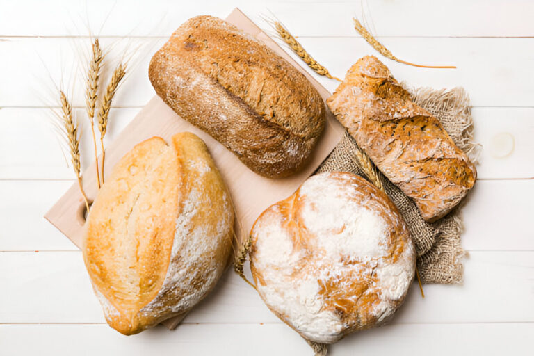 Various types of freshly baked bread displayed on a wooden surface with decorative wheat stalks.