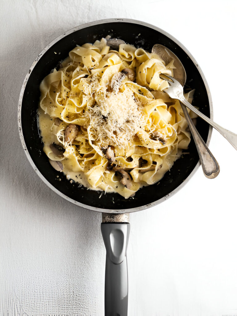 A frying pan filled with creamy pasta topped with grated cheese and black pepper.