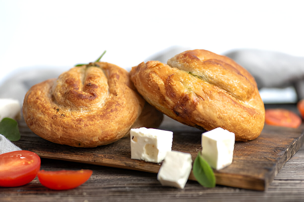 Two freshly baked rolls with cheese and sliced tomatoes on a wooden board.