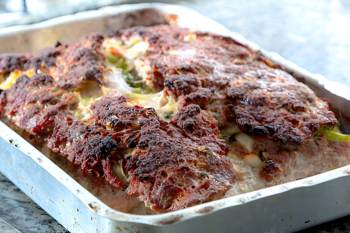 A baked meatloaf with a crispy top and visible vegetables peeking out, placed in a metal baking tray.