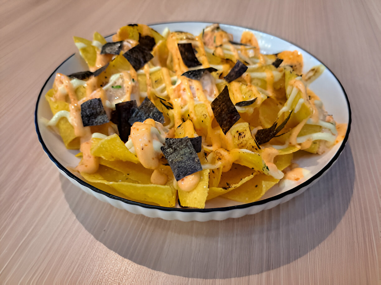 A plate of nachos topped with sauces and seaweed slices.