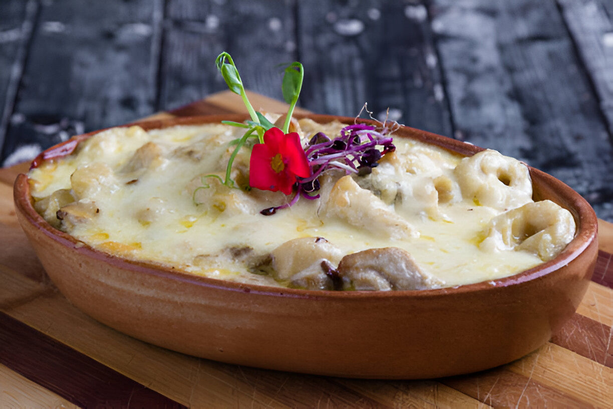 A baked dish in a brown ceramic casserole, topped with melted cheese, garnished with a red flower and purple sprouts.