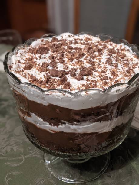 A glass bowl filled with layers of chocolate dessert, topped with whipped cream and chocolate shavings.