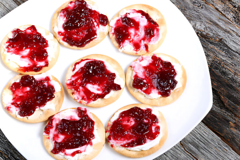 A plate of cream cheese and jelly topped crackers arranged neatly.