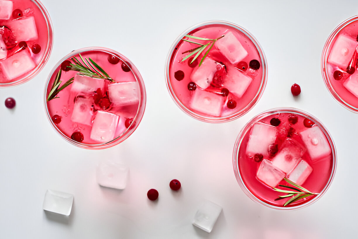 Colorful pink drinks with ice cubes and fresh berries in clear cups on a white background.