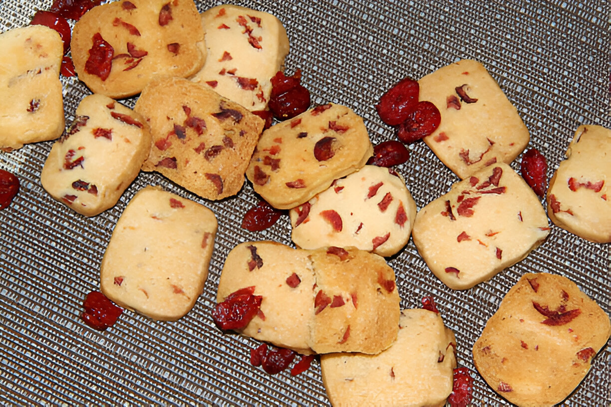 A variety of cookies with cranberries scattered on a textured surface.