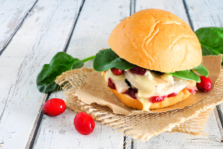 A close-up of a delicious sandwich filled with spinach, turkey, cranberry sauce, and melted cheese on a rustic wooden table.