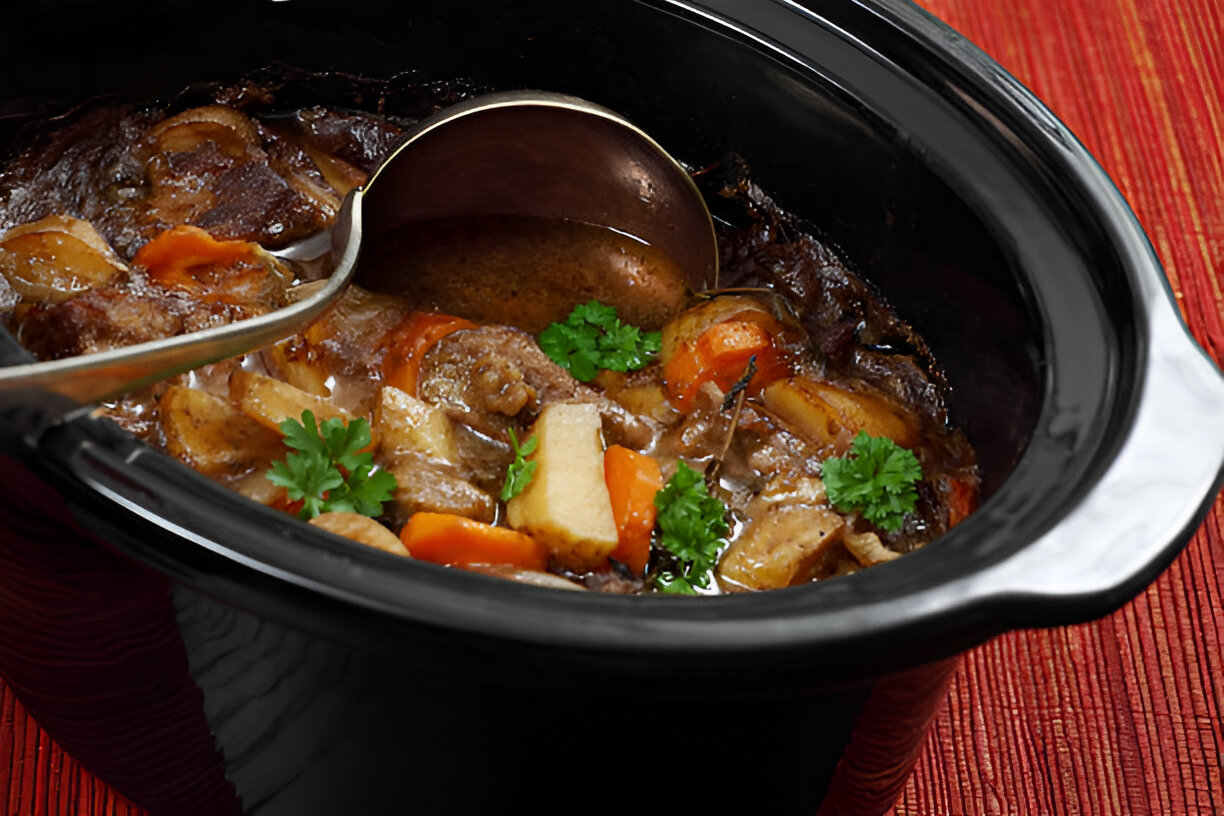 A close-up of a black slow cooker filled with a hearty meat and vegetable stew, garnished with fresh parsley.