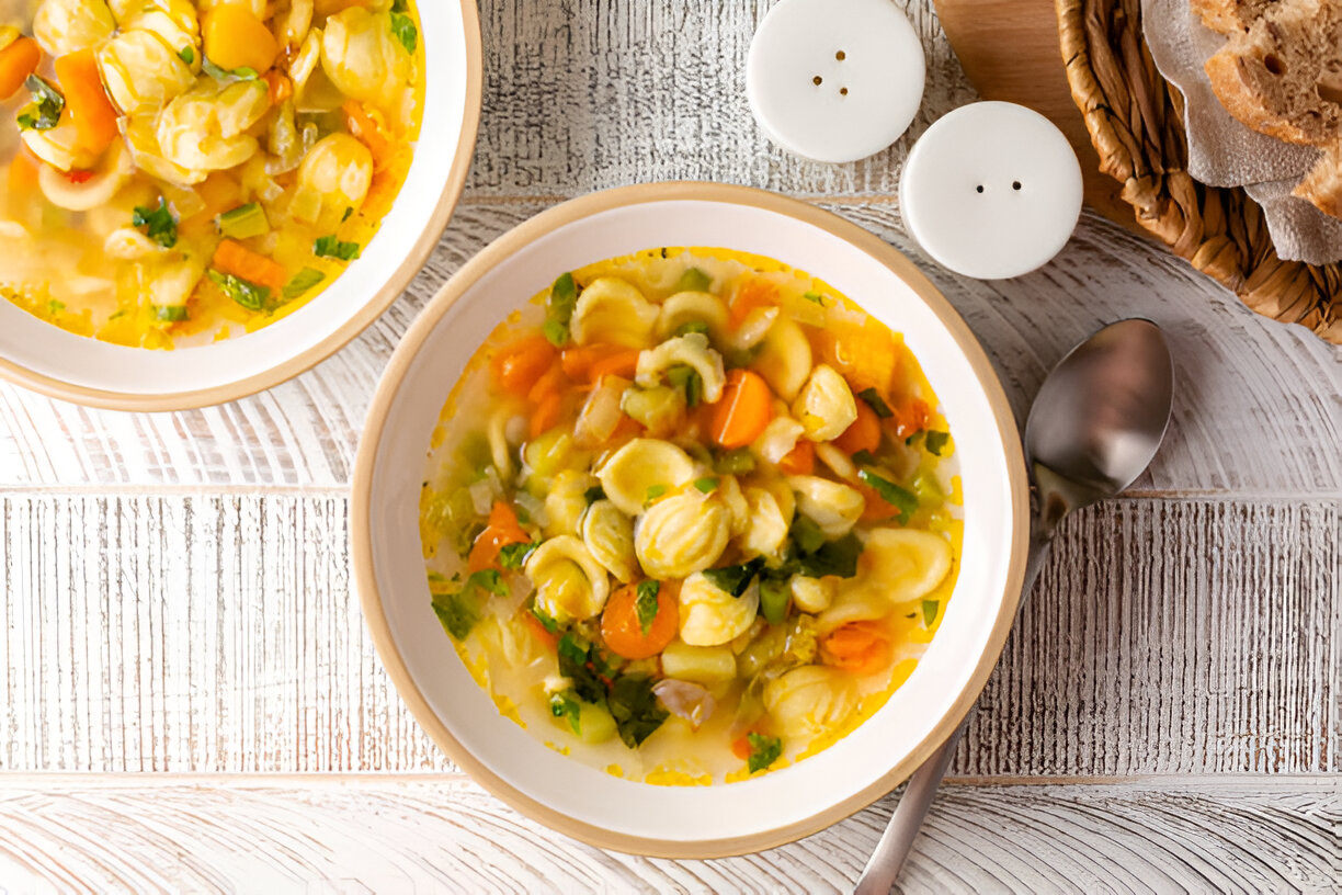 A hearty bowl of vegetable soup with pasta, garnished with fresh herbs, served in a light dish.
