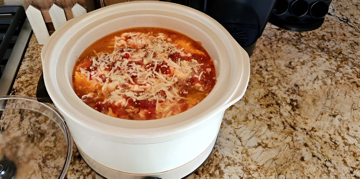 A slow cooker filled with a savory mixture of shredded chicken, tomatoes, and cheese, sitting on a granite countertop.