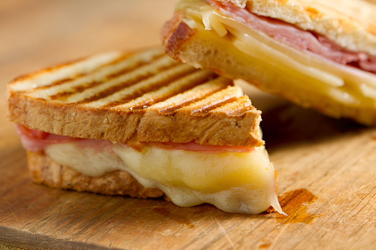 A delicious grilled sandwich with melted cheese and ham, cut in half and resting on a wooden surface.