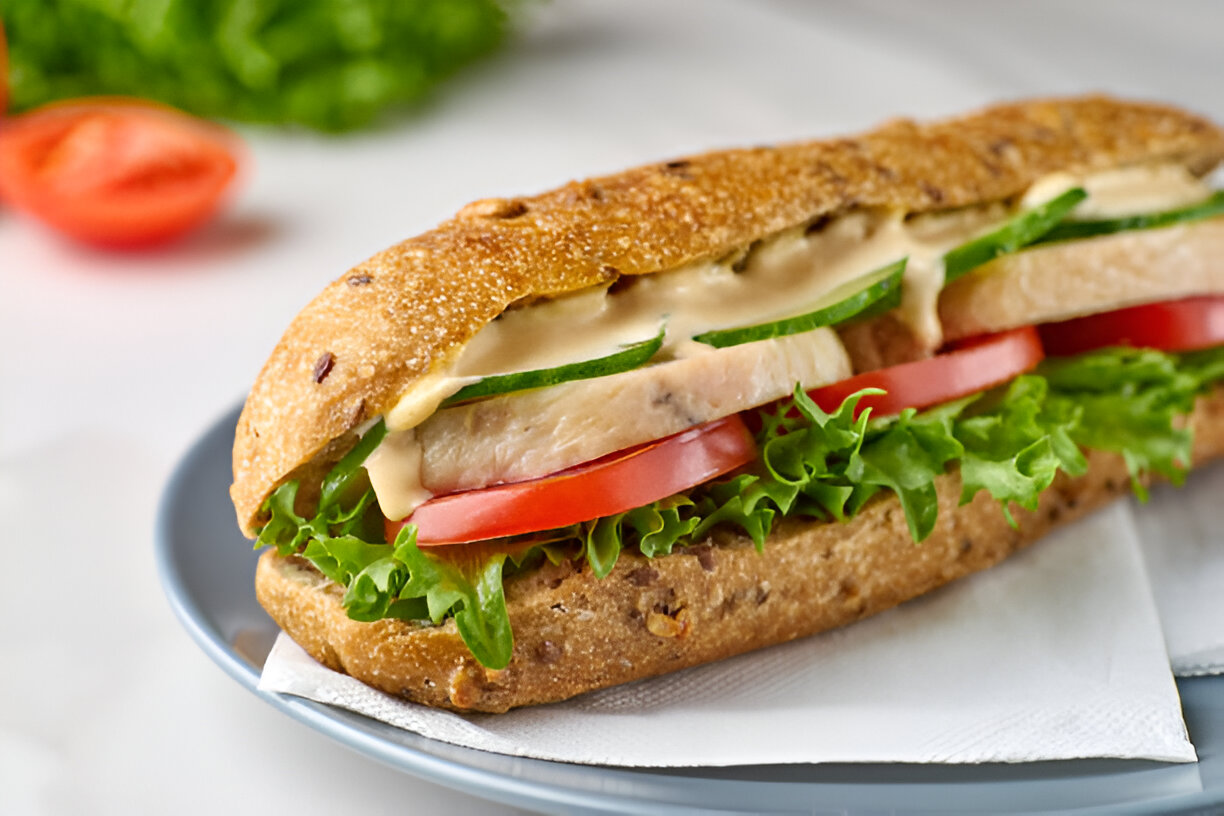 A delicious sandwich featuring slices of chicken, lettuce, tomato, and cucumber in a whole grain bun.