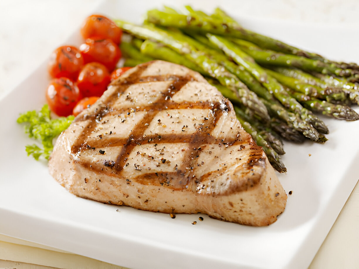 Grilled fish steak with asparagus and cherry tomatoes on a white plate