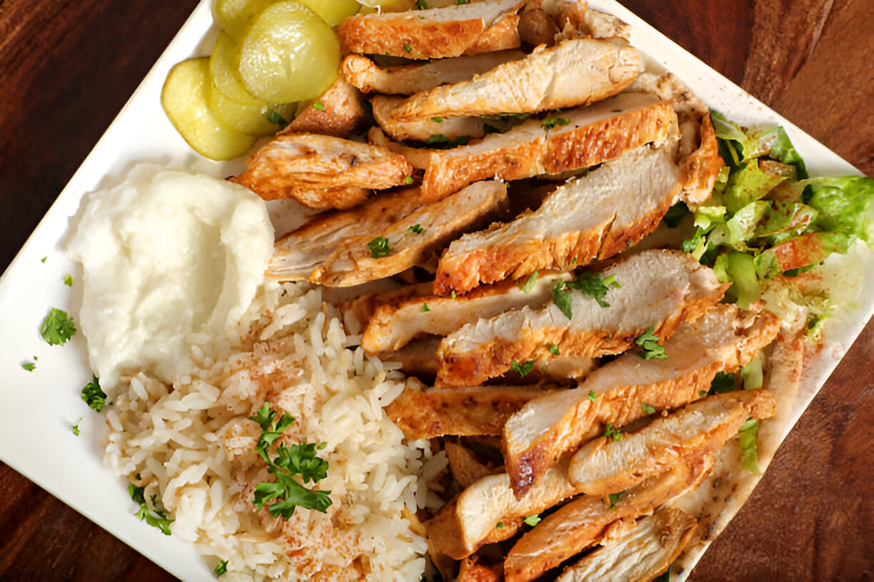 A plate of sliced grilled chicken served with rice, mashed potatoes, pickles, and salad.
