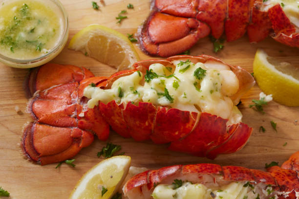 Grilled lobster tails topped with garlic butter and garnished with fresh herbs on a wooden cutting board.