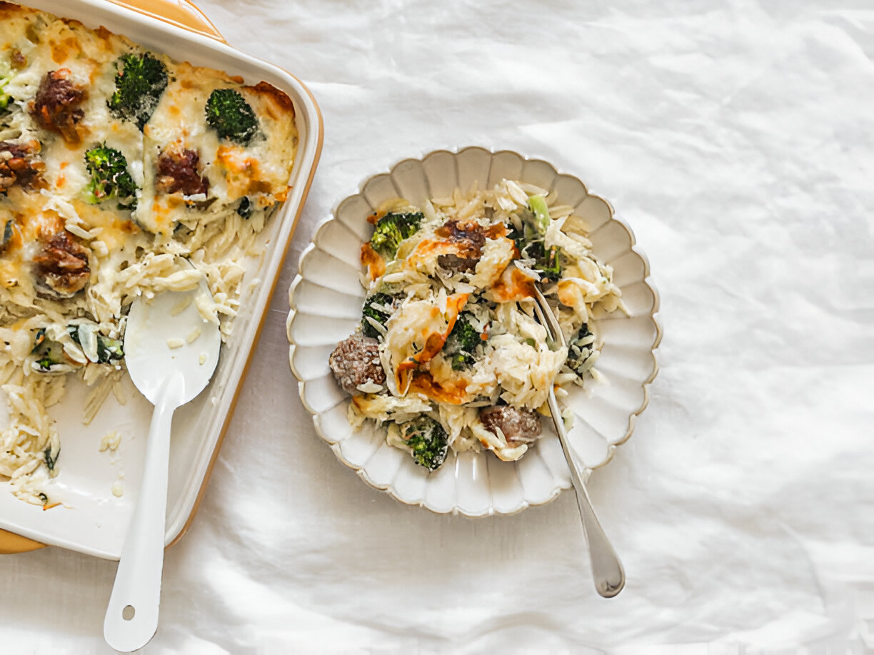 A creamy broccoli and sausage casserole served in a baking dish with a portion on a plate.