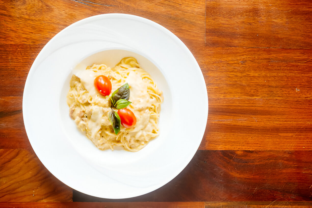 A plate of creamy pasta with cherry tomatoes and basil on a wooden table.