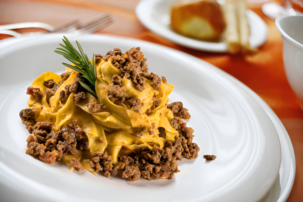 A plate of pasta topped with minced meat and garnished with a sprig of rosemary.