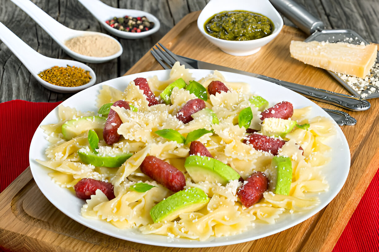 A plate of farfalle pasta with green apples and sausage, garnished with cheese and herbs, set on a wooden table.